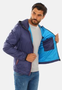 Giacca leggera blu navy con cappuccio, dotata di un interno azzurro brillante e tasche con zip. Tessuto liscio con dettagli di cucitura a contrasto.