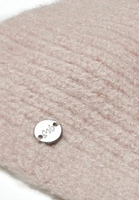 Soft pink knitted fabric with a textured finish, featuring a circular metallic tag with engraved initials, stitched into the fabric.