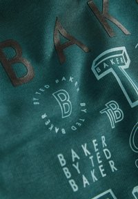 Teal kangas, millel on mitmeid trükitud logo erinevates suurustes ja värvides, sealhulgas "BAKER" ja "TED BAKER", tekstuuriga välimus.