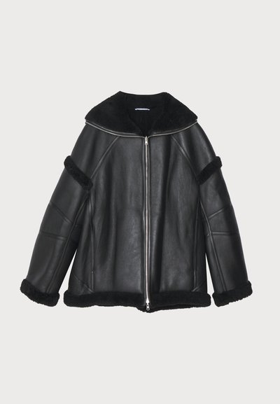 Black leather jacket with a zip front, wide collar, and shearling accents on the cuffs and hem, featuring a relaxed, boxy fit.