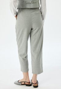 Pantalones gris claro, ajustados y con pierna cónica, con bolsillos traseros, combinados con elegantes zapatos negros tipo slingback texturizados. Acabado de tela suave.