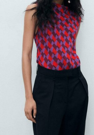 Mouwloze top met rood en paars geometrisch ruitpatroon, gecombineerd met een zwarte, hooggesneden geplooide broek op een persoon.