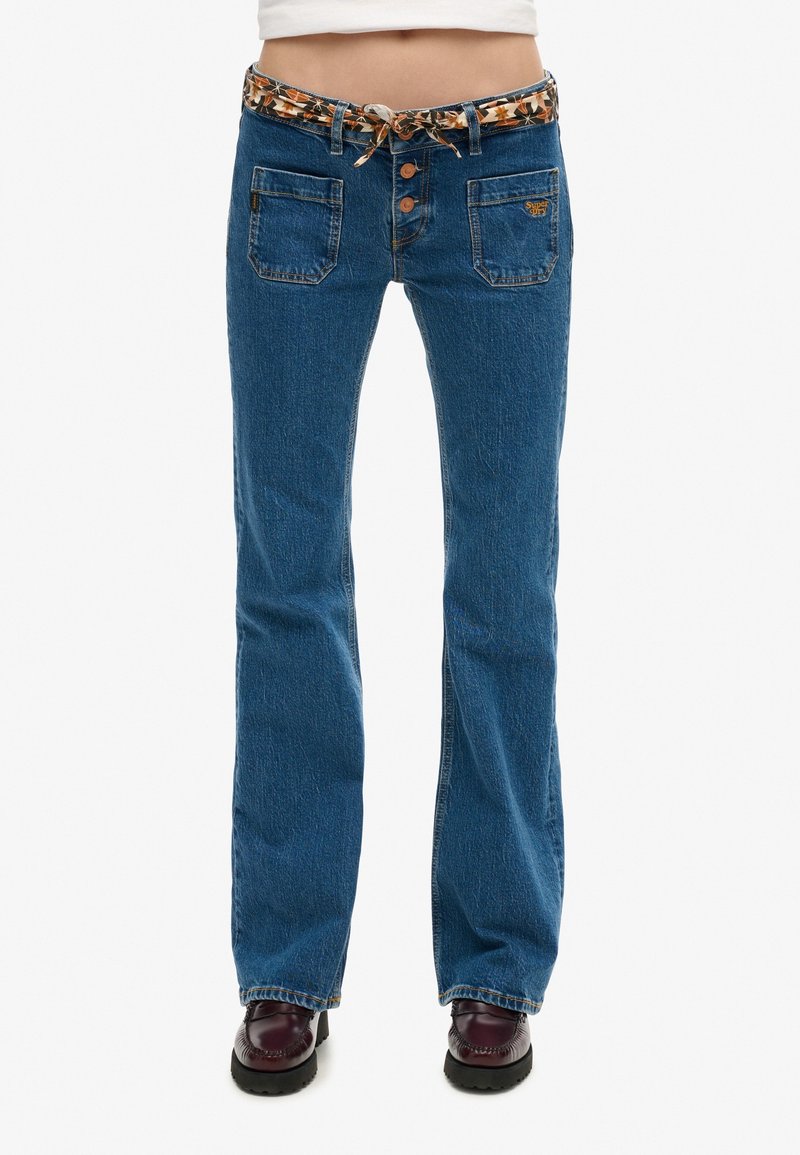 Jean flare en denim bleu moyen avec une ceinture en tissu à motifs et une fermeture à trois boutons. Comprend deux poches avant et une coupe régulière.