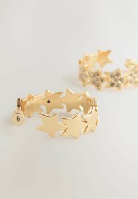 Brățară în formă de stea aurie, cu un design legat, textură netedă și închidere cu balama. Include un accent de strassuri pe o a doua brățară.