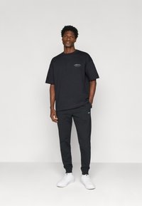 Czarna bawełniana koszulka z krótkim rękawem i małym logo; zestawiona z ciemnymi dresami i białymi trampkami. Prosty, sportowy design.