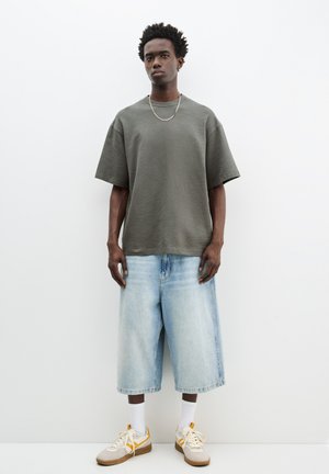 Olivengrøn, boxy bomulds t-shirt med brede ærmer, parret med lyseblå denim culottebukser. Tan sneakers med hvide og gule detaljer.