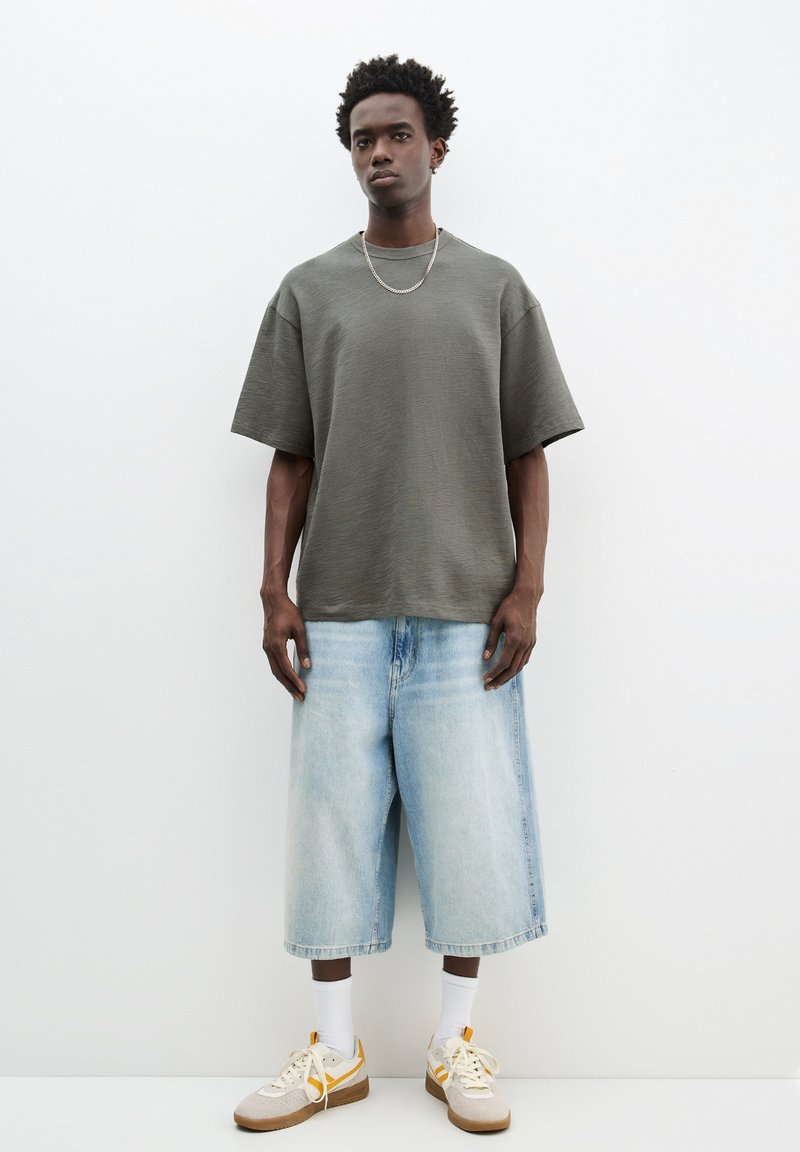 Olivengrøn, boxy bomulds t-shirt med brede ærmer, parret med lyseblå denim culottebukser. Tan sneakers med hvide og gule detaljer.