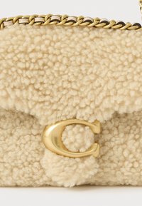 Krēmkrāsas, pūkaina tekstūra soma ar zelta ķēdes siksnu un zelta C formas aizdari priekšpusē. Kompakts taisnstūrveida formāts.