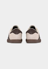 Set beige suède sneakers met donkerbruine hielkapjes en zolen, gezien van achteren op een effen witte achtergrond.