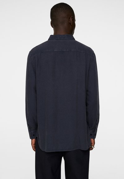 Dark navy long-sleeve shirt with a pointed collar, buttoned cuffs, and a smooth fabric texture. Hem is slightly rounded at the back.