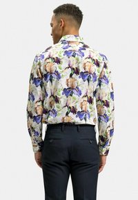 Blommig långärmad skjorta med lila och beige iris-mönster på vit bakgrund; kombinerad med svarta byxor för kontrast.