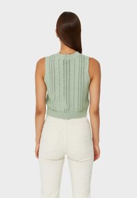 Mint green knitted sleeveless top with a ribbed texture and vertical perforations, paired with cream-colored high-waisted pants.