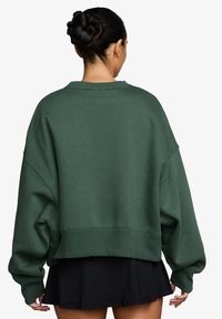 Sudadera verde de gran tamaño con cuello redondo, puños y dobladillo acanalados, hecha de una suave mezcla de algodón. Mostrada desde la parte posterior.