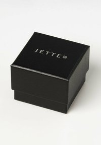 Sort faux læder kasse med en tekstureret overflade, forsynet med et sølvpræget logo "JETTE" på toppen, lukket klapdesign.