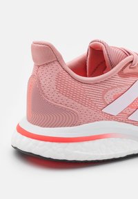 Chaussure de sport rose avec une tige en maille texturée, des accents blancs et une semelle amortie comportant une bande corail et un motif incurvé au talon.