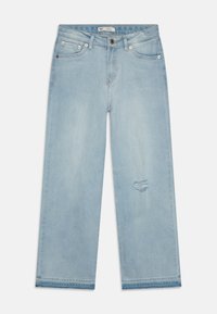 Jeans de tiro ancho de color azul claro, hechos de denim, con una zona desgastada en la pierna derecha y herrajes estándar con cinco bolsillos.