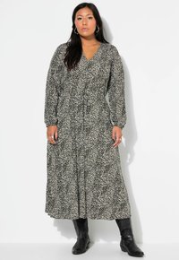 Schwarz-weißer gemusterter Maxikleid mit langen Ärmeln, V-Ausschnitt, tailliertem Bund und flatterndem Rock; kombiniert mit schwarzen Stiefeln bis zu den Knien.