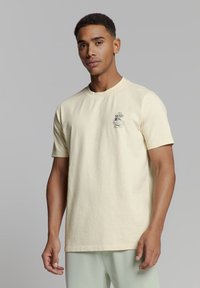 Lichtgele katoen t-shirt met korte mouwen, voorzien van een kleine grafische afbeelding op de linkerborst en een ontspannen pasvorm. Effen textuur.