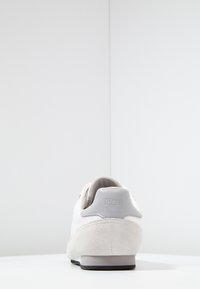 Vita lädersneakers med grå mockadetaljer, rund tå och en strukturerad sula. Har en prägling av logotypen på hälen.