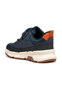Zapatilla deportiva en azul marino y negro con suela blanca resistente, lengüeta trasera naranja y correa de Velcro, mostrada desde un ángulo trasero.