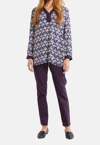 Maglietta a maniche lunghe con motivo a foglie blu navy e crema, scollo a V; pantaloni blu navy abbinati con pois rossi; abbinati a scarpe basse nere.