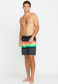 Shorts de bain noirs avec un dégradé de rose, vert et jaune ; dotés de rayures horizontales blanches et d'un cordon de serrage à l'avant pour l'ajustement.