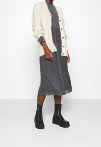 Kremowy sweter dzianinowy z prążkowanym wzorem na czarnej i białej wzorzystej sukience. Czarne wojskowe buty za kostkę z masywną podeszwą.