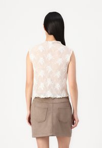 Top sem mangas, na cor creme, com padrão floral texturizado e bainha recortada, combinado com uma saia mini em camurça taupe com bolsos traseiros.