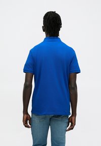 Kék galléros póló rövid ujjú, sima textúrájú, világoskék farmerral viselve. Nincsenek látható minták vagy logók.