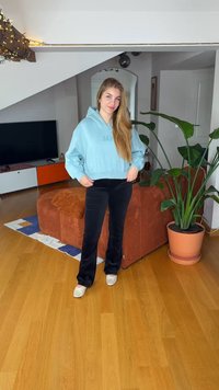 Φωτεινό γαλάζιο cropped φούτερ με λογότυπο "GAP", σε συνδυασμό με μαύρο βελούδινο παντελόνι με φαρδιά γραμμή και ανοιχτόχρωμα παπούτσια, στέκεται σε ξύλινο δάπεδο.