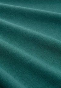 Morska bawełniana tkanina o gładkiej, matowej teksturze, z delikatnymi fałdami i jednolitą powierzchnią. Brak widocznych wzorów lub ozdób.