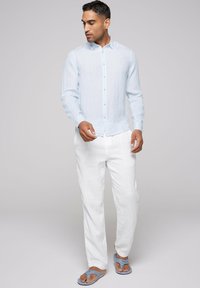 Camisa de lino azul claro de botones con mangas largas, combinada con pantalones de lino blancos y sandalias azules. La camisa presenta un tejido texturizado.