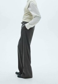 Pantalons gris à jambes larges avec un gilet en tricot texturé crème par-dessus une chemise blanche. Comprend des poches latérales et une coupe décontractée.