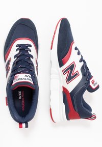 Baskets pour hommes avec une tige en textile bleu marine et blanc, accents rouges, fermeture à lacets, col rembourré et semelle extérieure blanche. Logo visible.