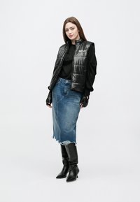 Γυναίκα που φοράει μαύρο αμάνικο μπουφάν, μαύρο μακρυμάνικο τοπ, τζιν μίντι φούστα με ξεφτισμένο τελείωμα, μαύρα γάντια και μαύρες μπότες με τακούνι μέχρι το γόνατο.