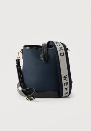 Τσαντάκι κάδου από ύφασμα σε ναυτικό μπλε με μαύρη δερμάτινη διακόσμηση και ρυθμιζόμενο λουρί, με φαρδύ μπλε και λευκό λουρί ώμου με κείμενο.