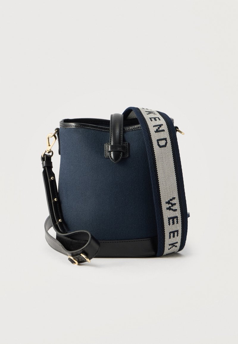 Τσαντάκι κάδου από ύφασμα σε ναυτι κό μπλε με μαύρη δερμάτινη διακόσμηση και ρυθμιζόμενο λουρί, με φαρδύ μπλε και λευκό λουρί ώμου με κείμενο.