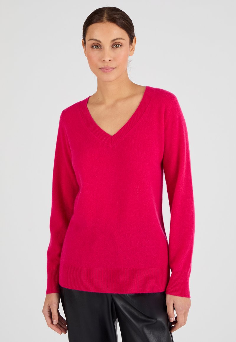 Pull over rose en V fabriqué dans un matériau doux, avec des manches longues et des bords côtelés. Texture lisse avec une coupe décontractée.