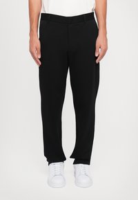 Zwarte, ruime broek met een platte voorkant, riemlussen en zijzakken, gecombineerd met witte sneakers. Textuurstof.