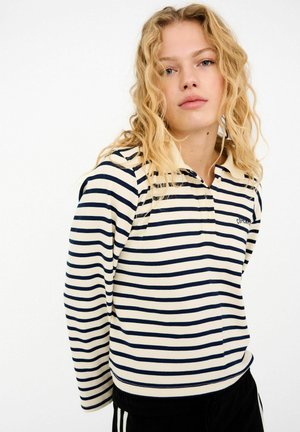 Tricou polo cu mânecă lungă în dungi, în nuanțe de crem și albastru închis. Are guler, fante cu nasturi și un logo mic pe piept. Textură moale a țesăturii.