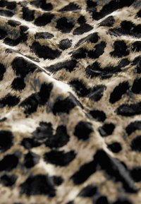 Leopardo rašto audinys, pasižymintis aksominiu tekstūros paviršiumi, su smėlio spalvos fonu ir ryškiomis juodomis dėmėmis skirtingų dydžių.