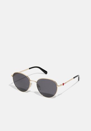Gold-framed sunglasses with grey lenses, oval shape, featuring black temple tips and a red accent detail on the right side.