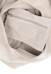 Beige Wildledertasche mit einem Innenraum, der ein Reißverschlussfach aufweist, das mit einem strukturierten Innenfutter und einem mit Nähte versehenen Etikett ausgestattet ist. Kettendetails am Reißverschlusszieher.