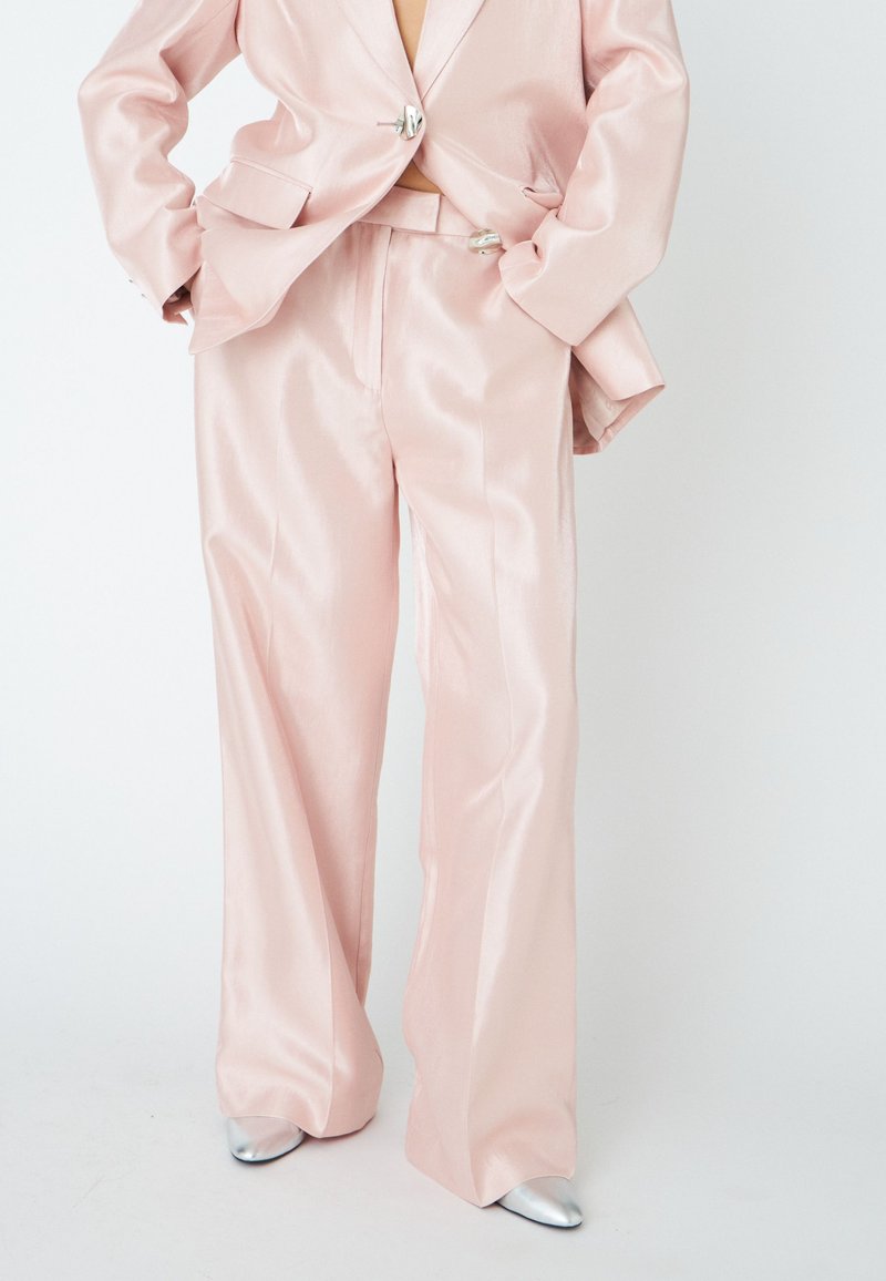 Light pink satin blazer and wide-leg trousers with a slightly glossy finish; features silver buttons and pointed silver shoes.