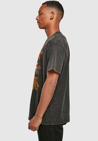 Camiseta de gran tamaño en gris oscuro con un estampado gráfico que presenta colores brillantes. Manga corta, cuello redondo y un corte relajado. Material de algodón.