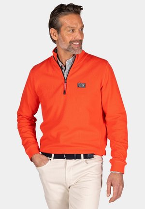 Oranje rits-jersey gemaakt van textiel met textuur, met een hoge kraag en een logo-opdruk op de borst. Draagt over een bedrukt shirt.
