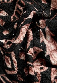 Teksturēta auduma melnā krāsā ar rozā un bēša ģeometriskiem rakstiem, ar sakrumdētu virsmu un izteiksmīgām formām.