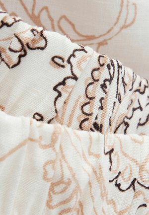 Close-up of beige and black floral embroidery on cream-colored textured fabric with gathered pleats.