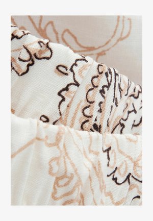 Close-up of beige and black floral embroidery on cream-colored textured fabric with gathered pleats.
