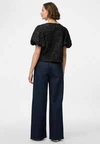 Svart topp med puffärmar i texturerad tyg, kombinerad med vida mörkblå denimjeans som har klassiska fickor och en liten flare vid fållen.